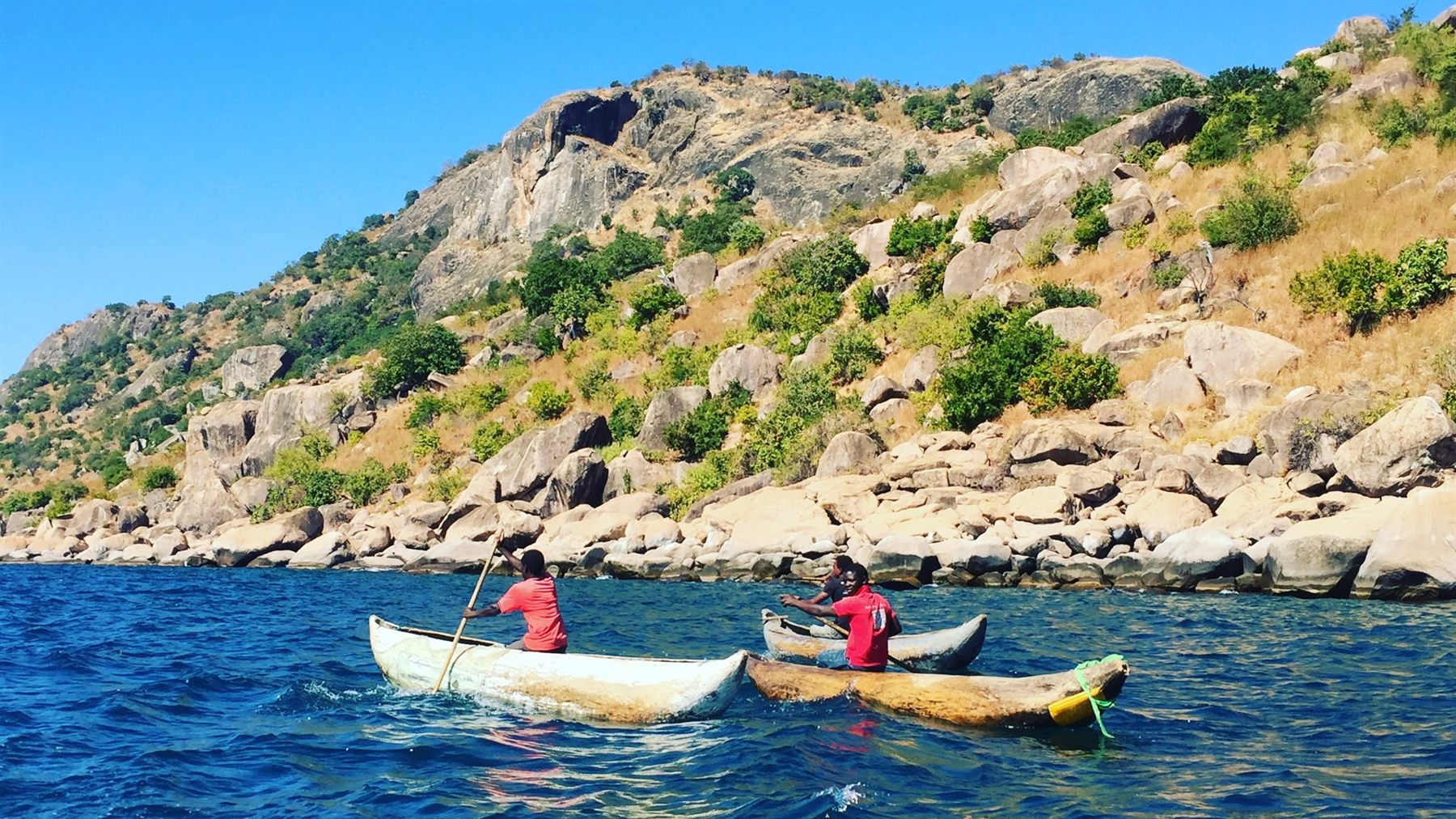 Two hand-built dugout canoes paddled between rocky islands on Lake Malawi