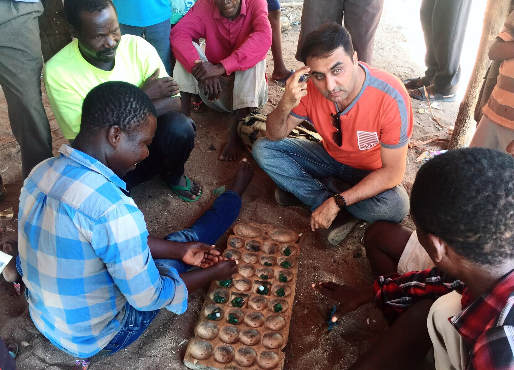 PMEye researcher seated on the ground playing a bao board game with a group of community members in Malawi