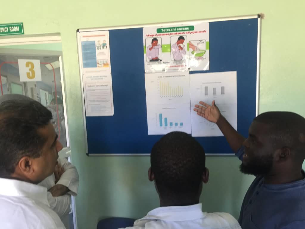 PMEye consultant and health facility staff reviewing service data charts pinned to a notice board at a health facility in Malawi