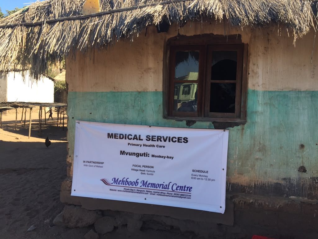 Primary health care outreach point at Mvunguti, Monkey Bay, Malawi, with a medical services banner outside a village building