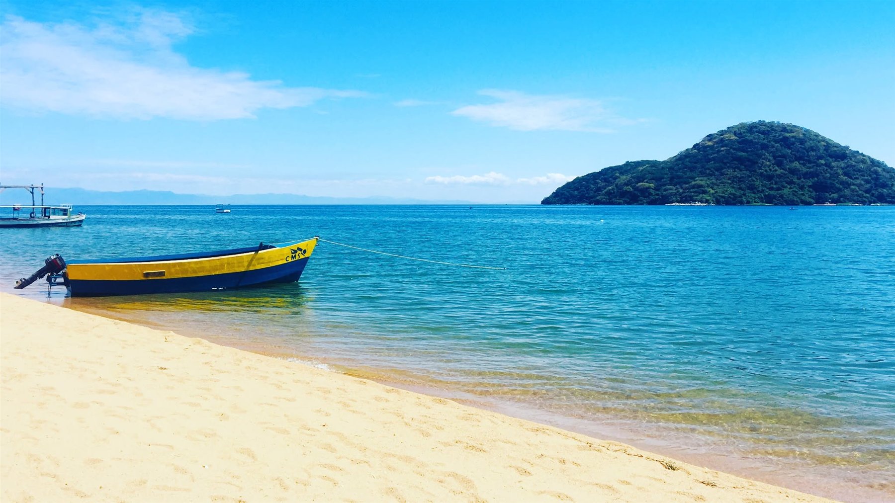 Boat moored at a sandy shore on Lake Malawi with a forested island in the distance