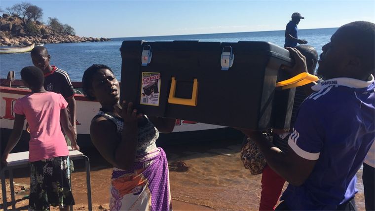 Field team carrying a supply trunk ashore at a settlement without road access