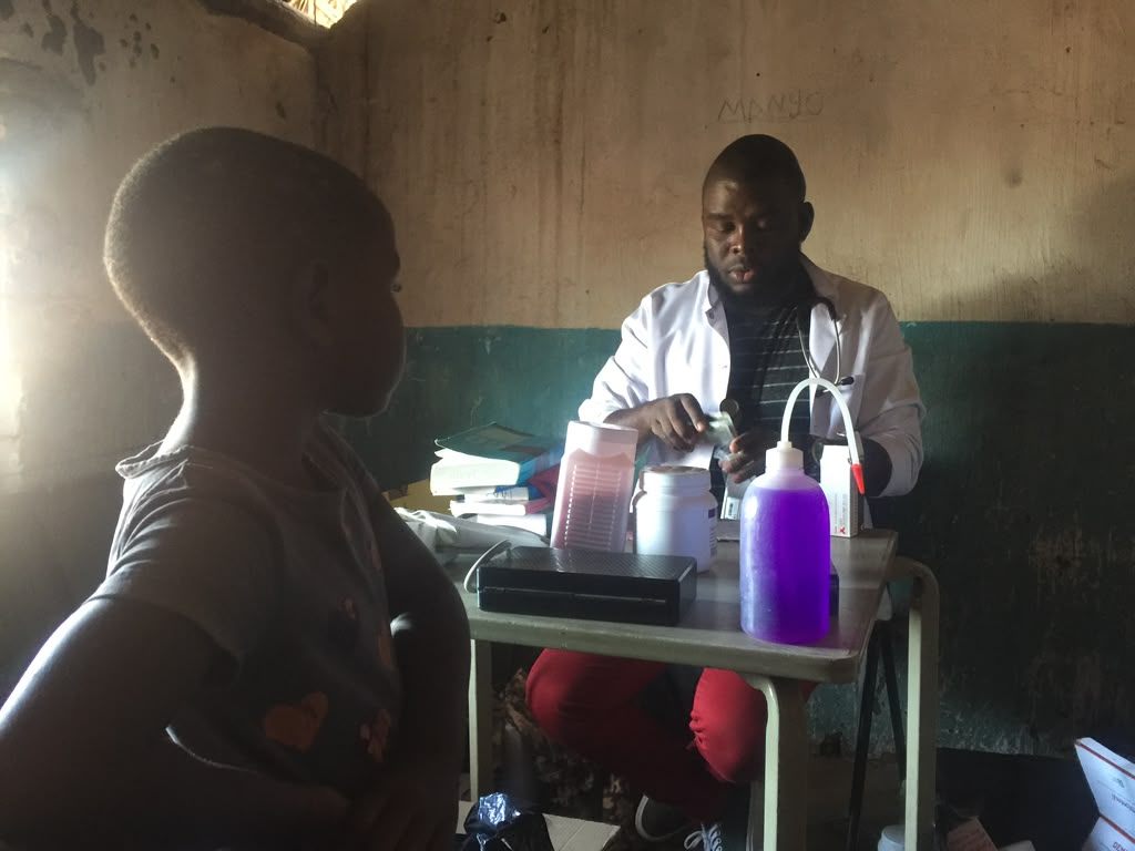 Clinician with a stethoscope preparing medication during a consultation at a rural health facility in Malawi