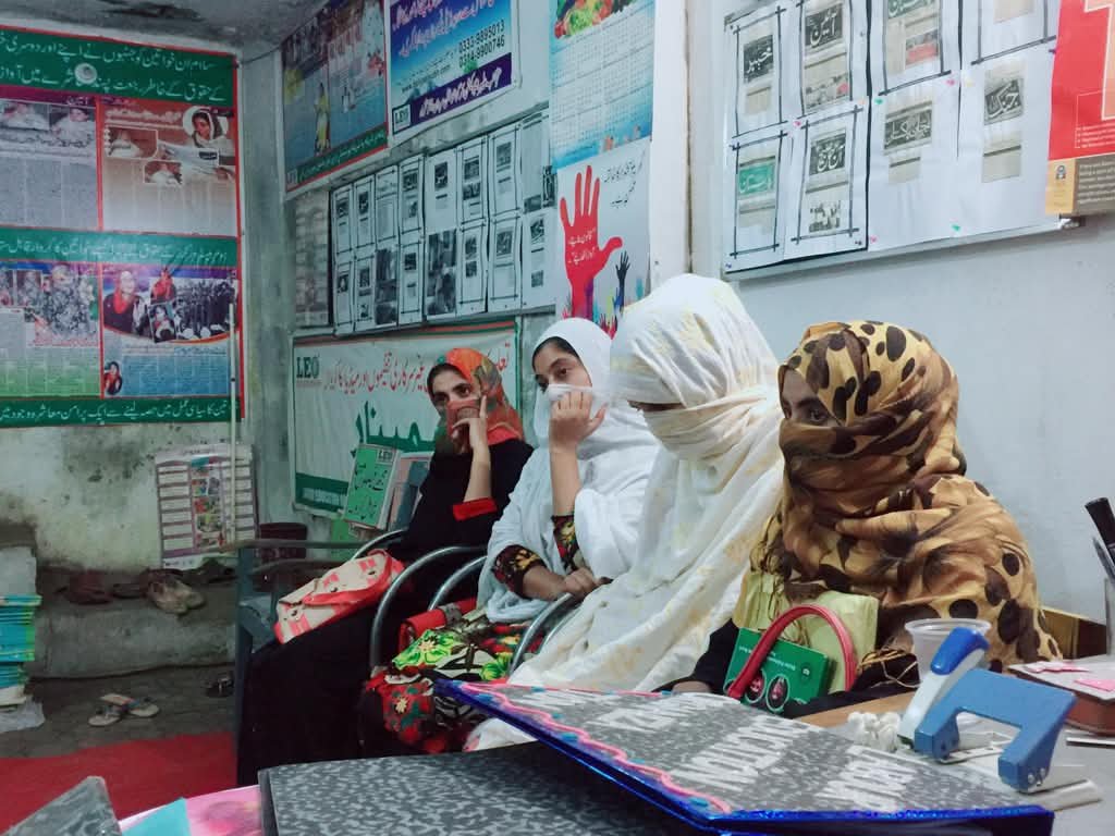 Women field staff seated together during a proposal writing training in a Labour Education Organization office in Mardan, with campaign material on the walls behind them